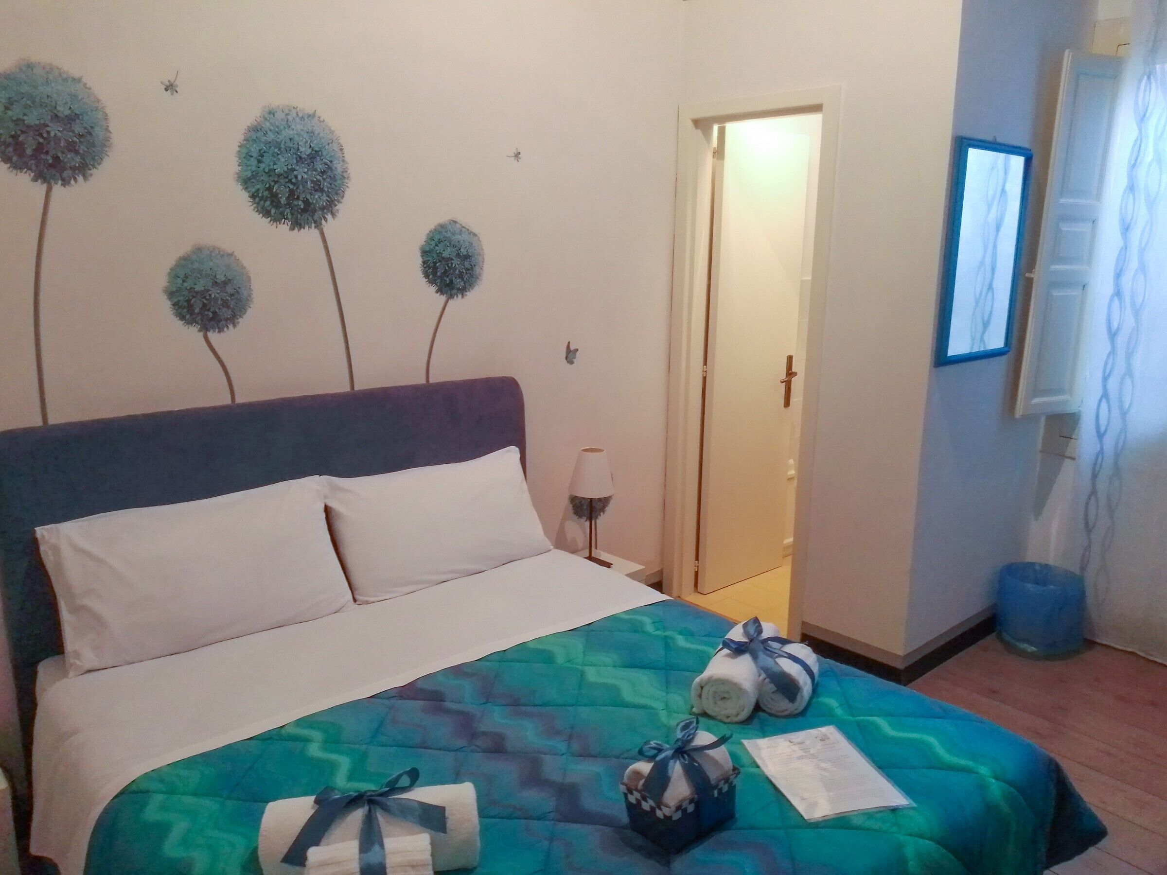 A neatly made bed with a blue and green patterned bedspread, two rolled towels with blue ribbons, and a white pillow.