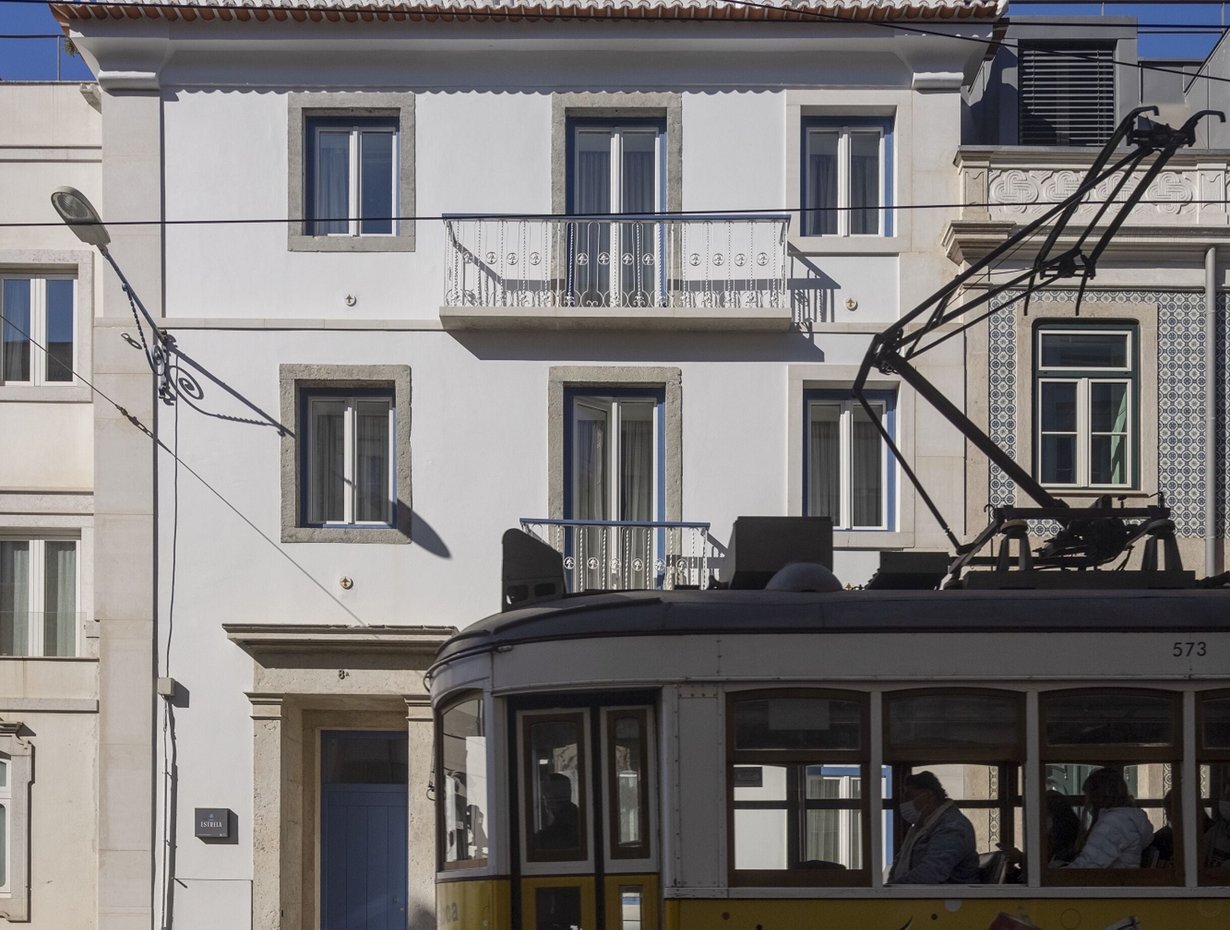 Un tranvía con pasajeros, un edificio con balcones y un letrero que dice 'ESTELLA'.
