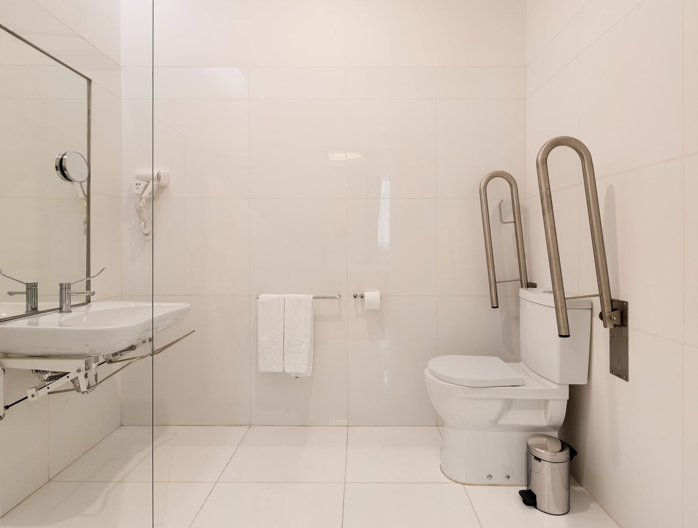 Une salle de bain moderne avec une douche à parois de verre, un lavabo blanc et des toilettes équipées d’une barre d’appui.