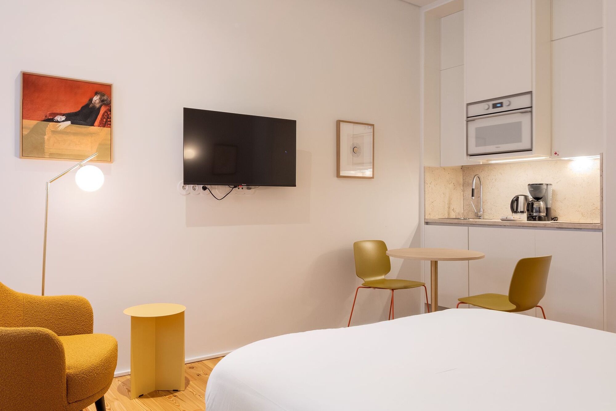 A hotel room with a bed, a TV, a small kitchen area, and two chairs.
