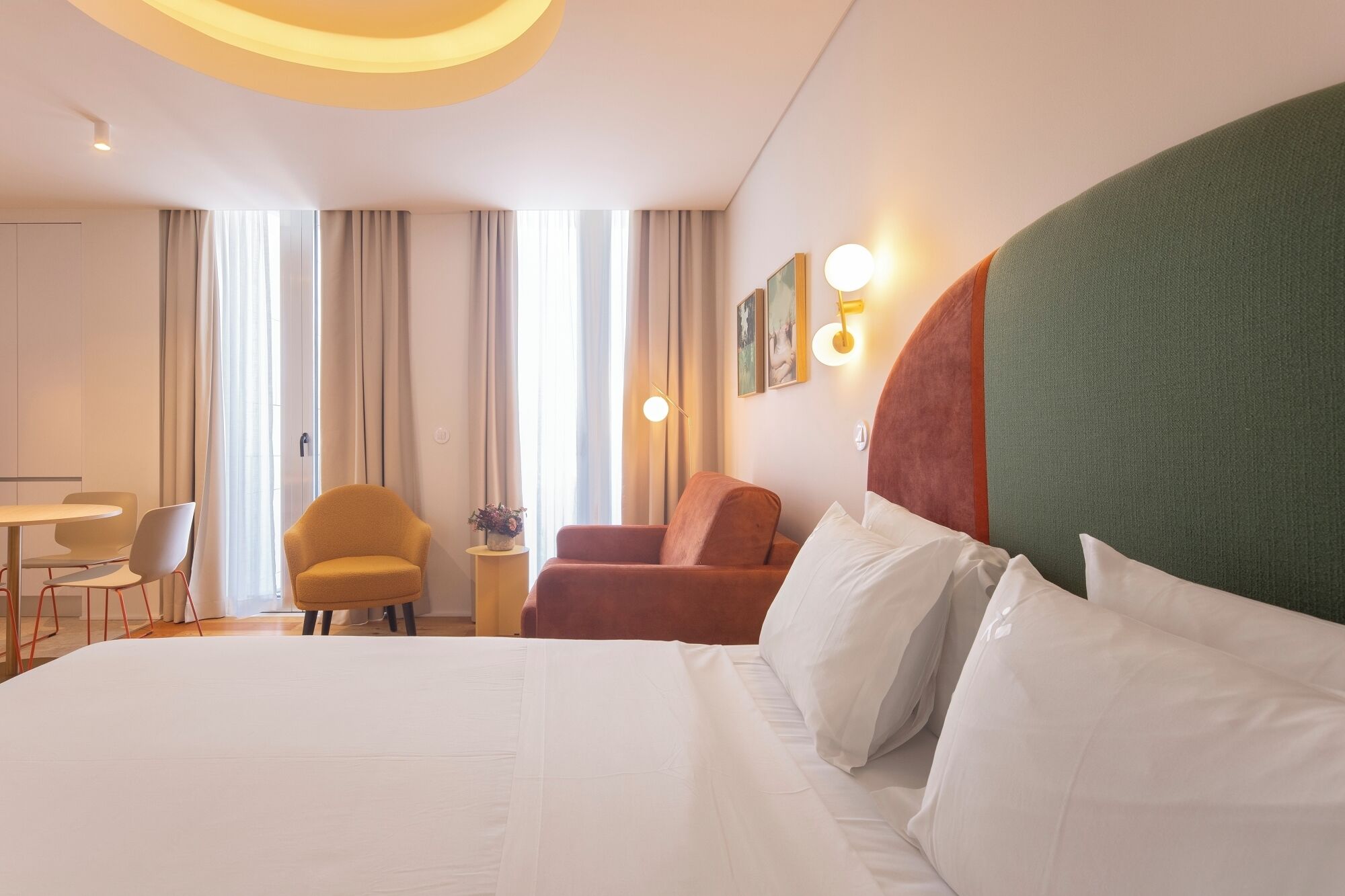 A hotel room with a large bed, a desk, two chairs, and a small table with a vase.