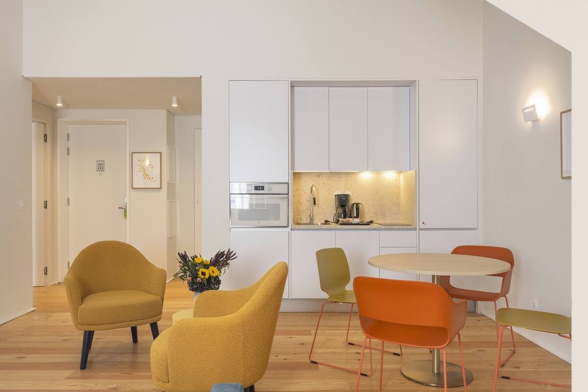 A modern kitchen with built-in appliances, a dining area with a round table and chairs, and a hallway leading to a door.
