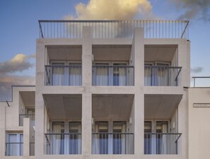 A multi-story building with balconies, large windows, and a clear sky.