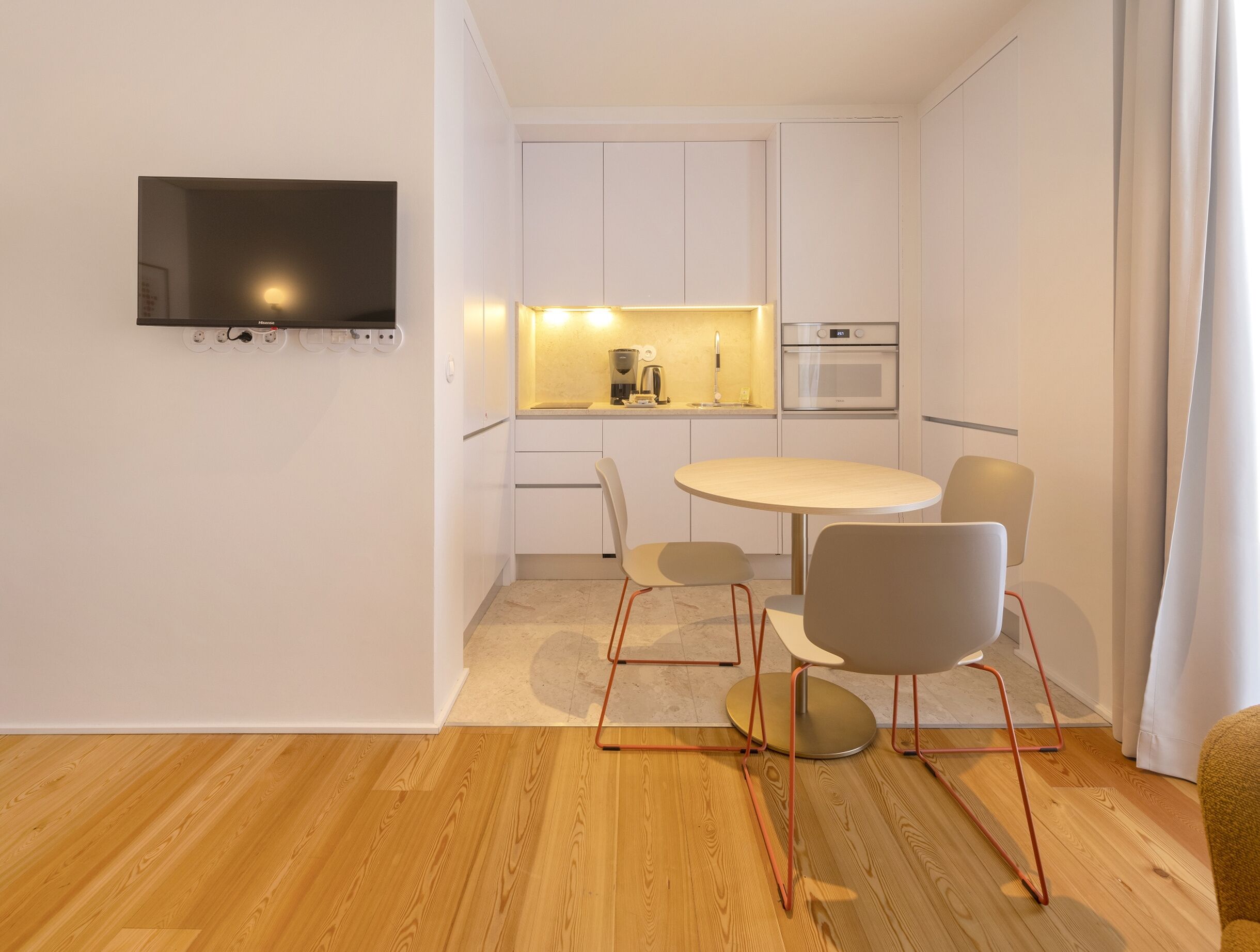 Una cocina moderna con armarios blancos, horno empotrado y una mesa de comedor redonda con sillas.