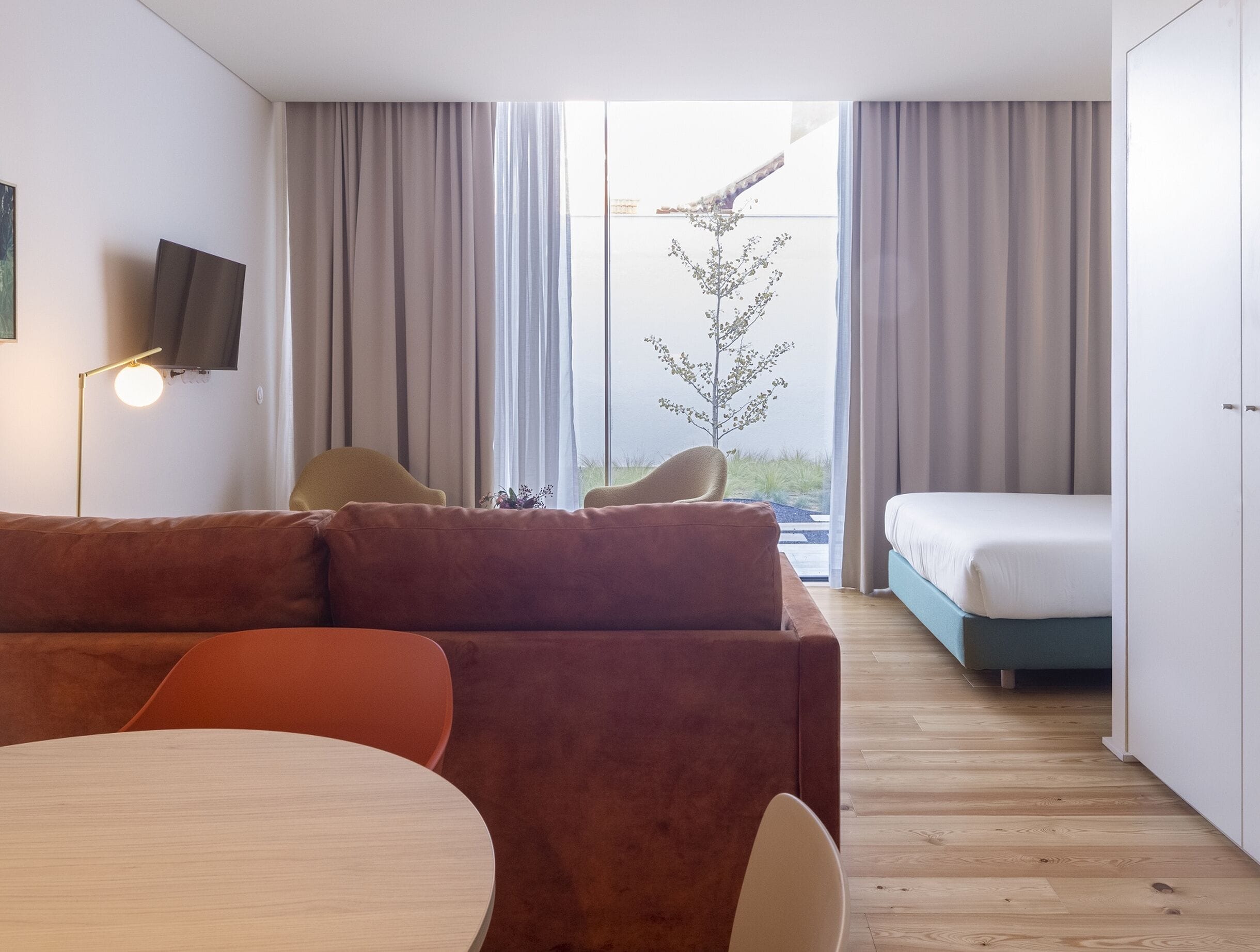 A modern room with a brown sofa, a small round table, a bed, and a TV mounted on the wall.