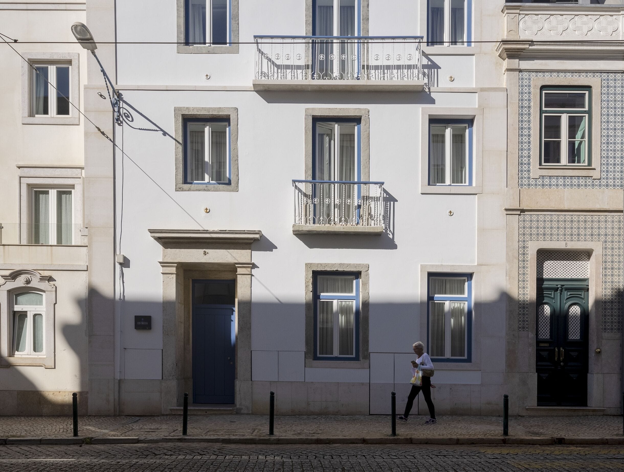 A building with multiple windows, a central entrance, and a person walking on the street.