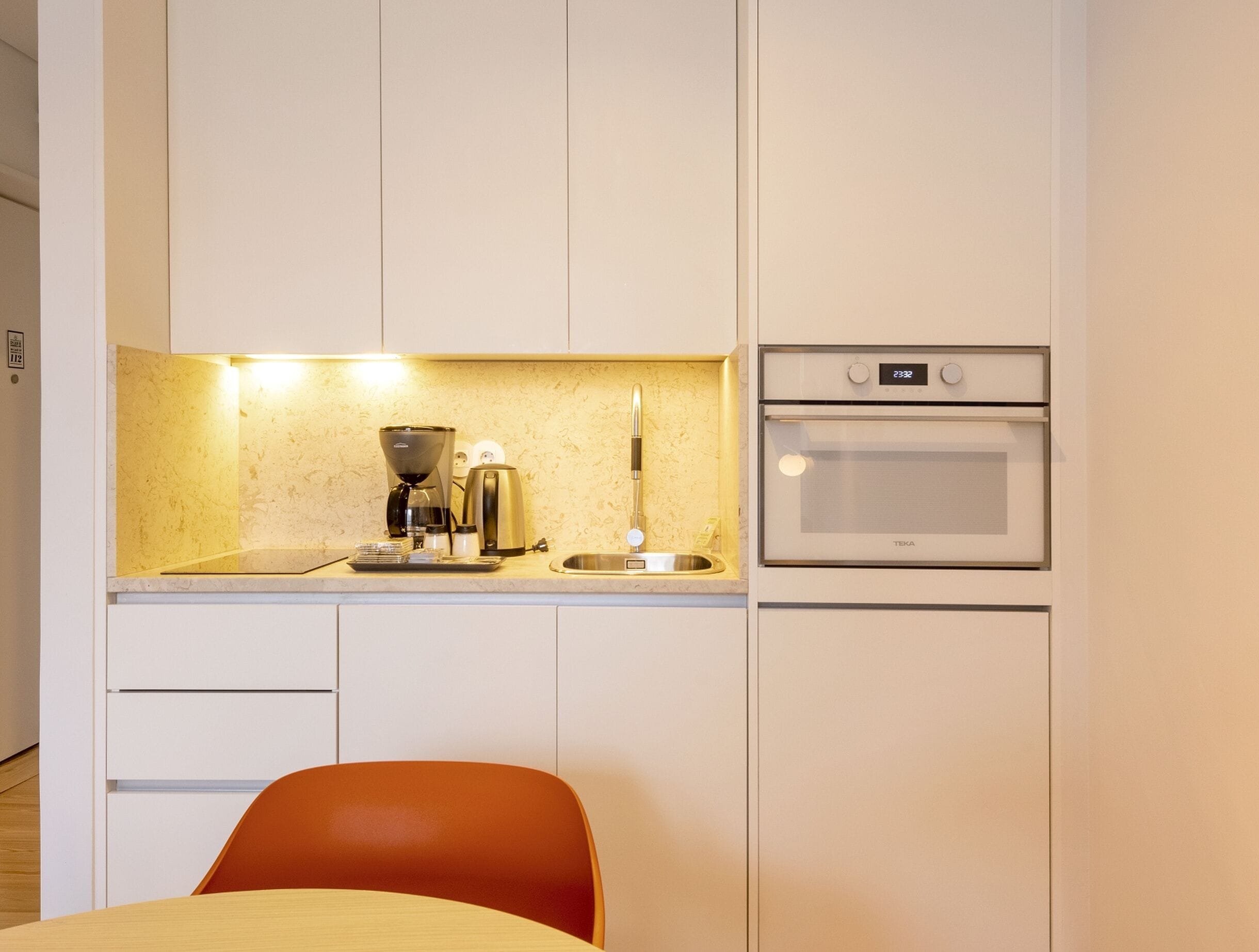 A compact kitchen with a coffee maker, kettle, and oven.