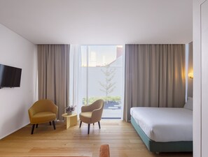 A hotel room with a bed, two armchairs, a small table with a vase, and a TV mounted on the wall.