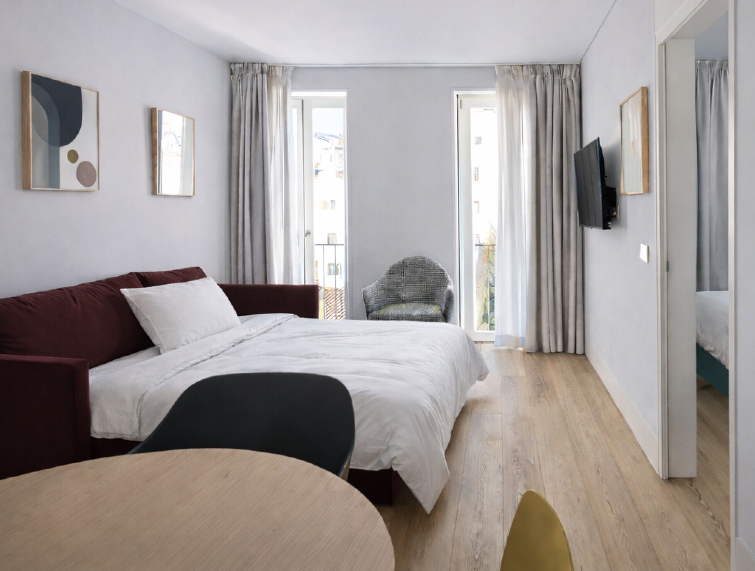 A modern hotel room with a bed, a sofa, a chair, a table, and a TV.