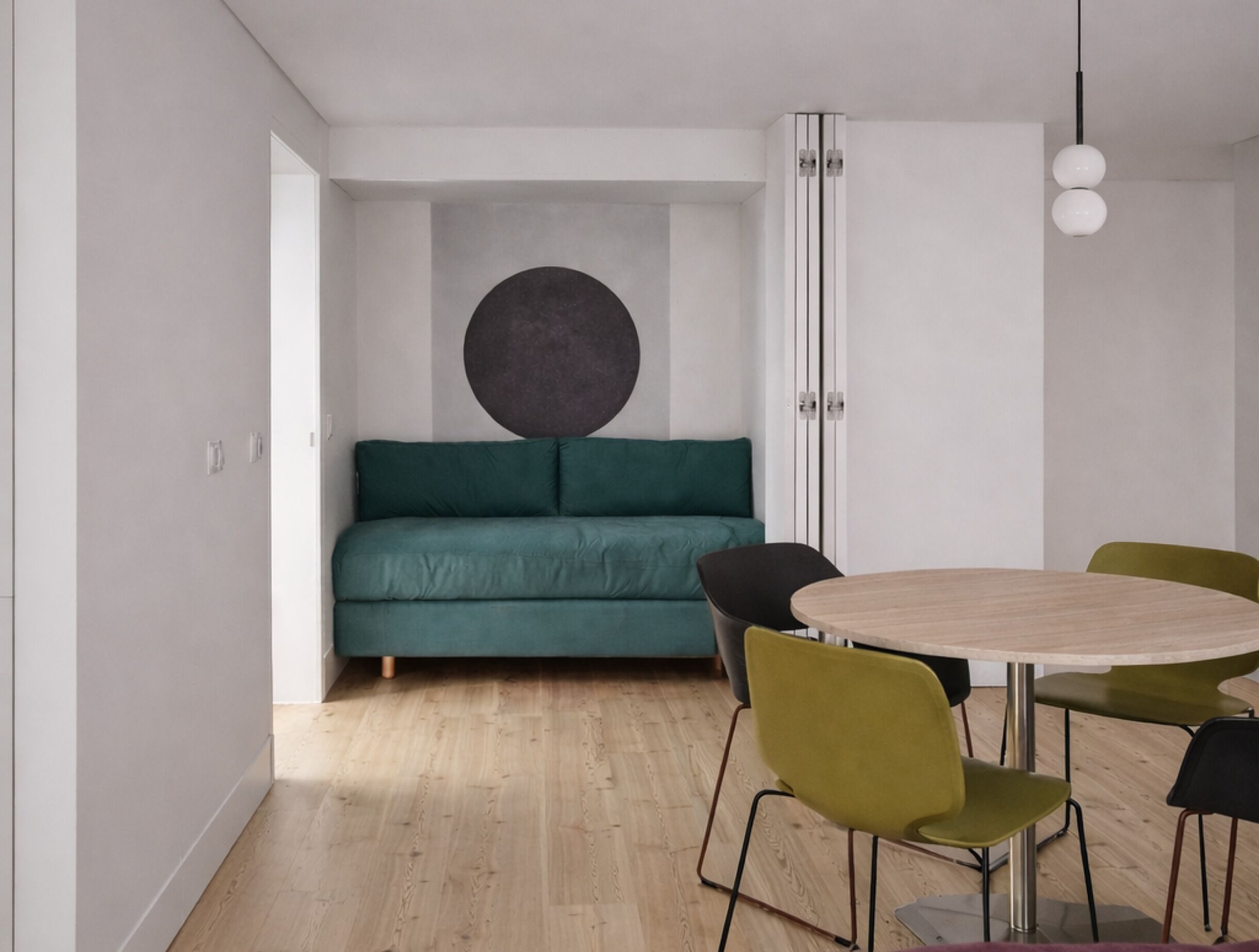 A modern room with a green sofa, a round table with chairs, and a large circular wall decoration.