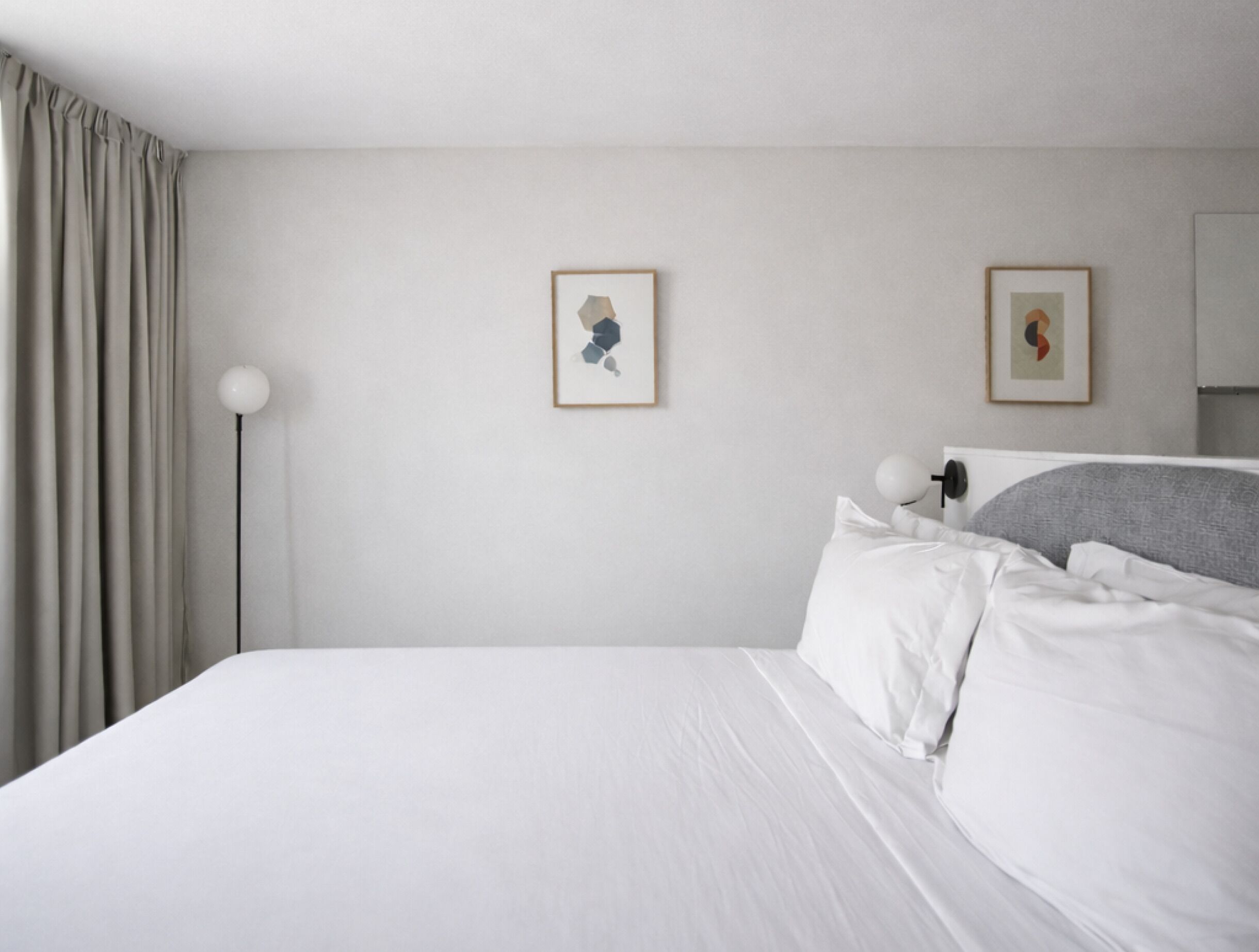 Een hotelkamer met een netjes opgemaakt bed, een vloerlamp en twee ingelijste kunstwerken aan de muur.