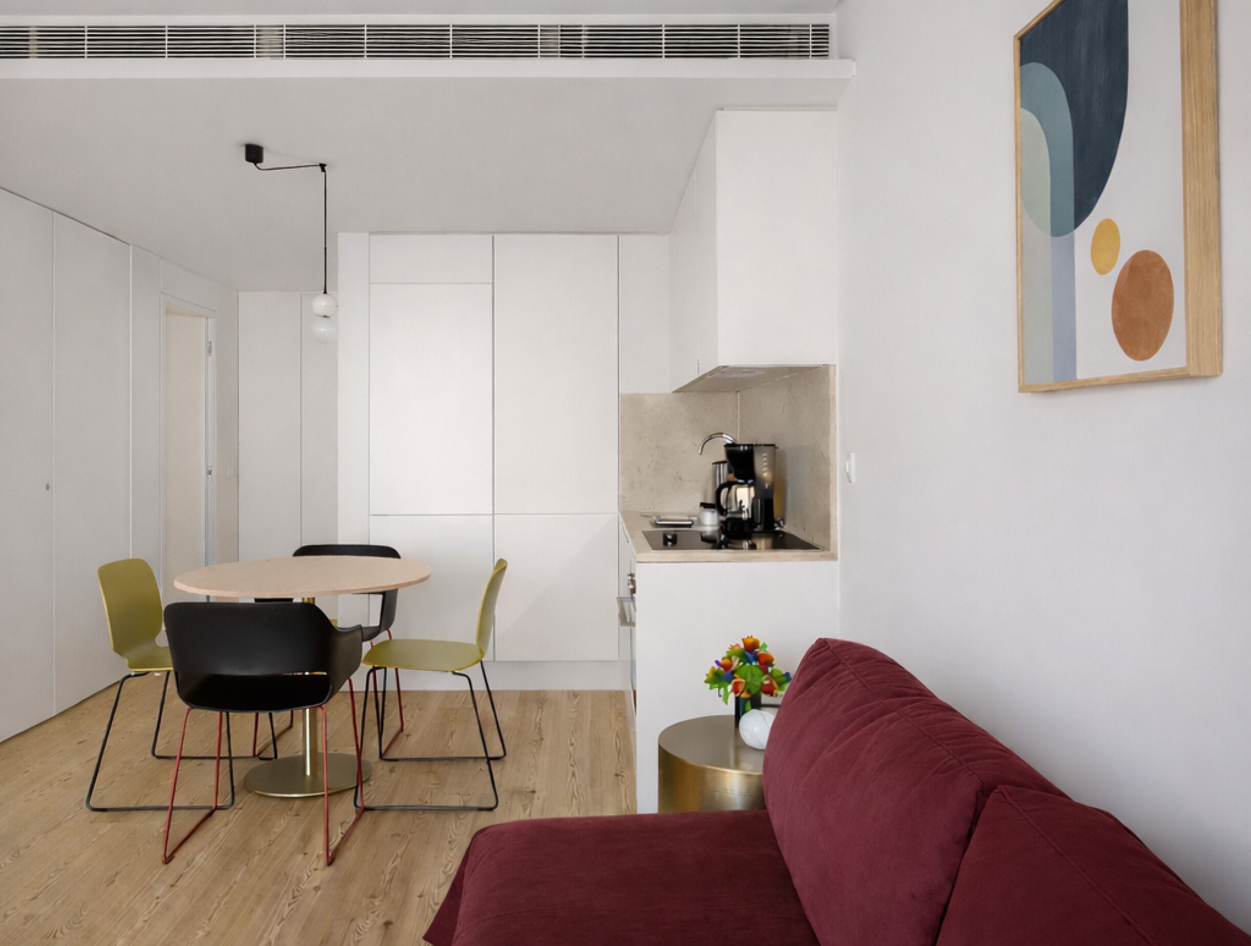 A modern living space with a dining area, a sofa, a coffee machine, and a wall-mounted artwork.