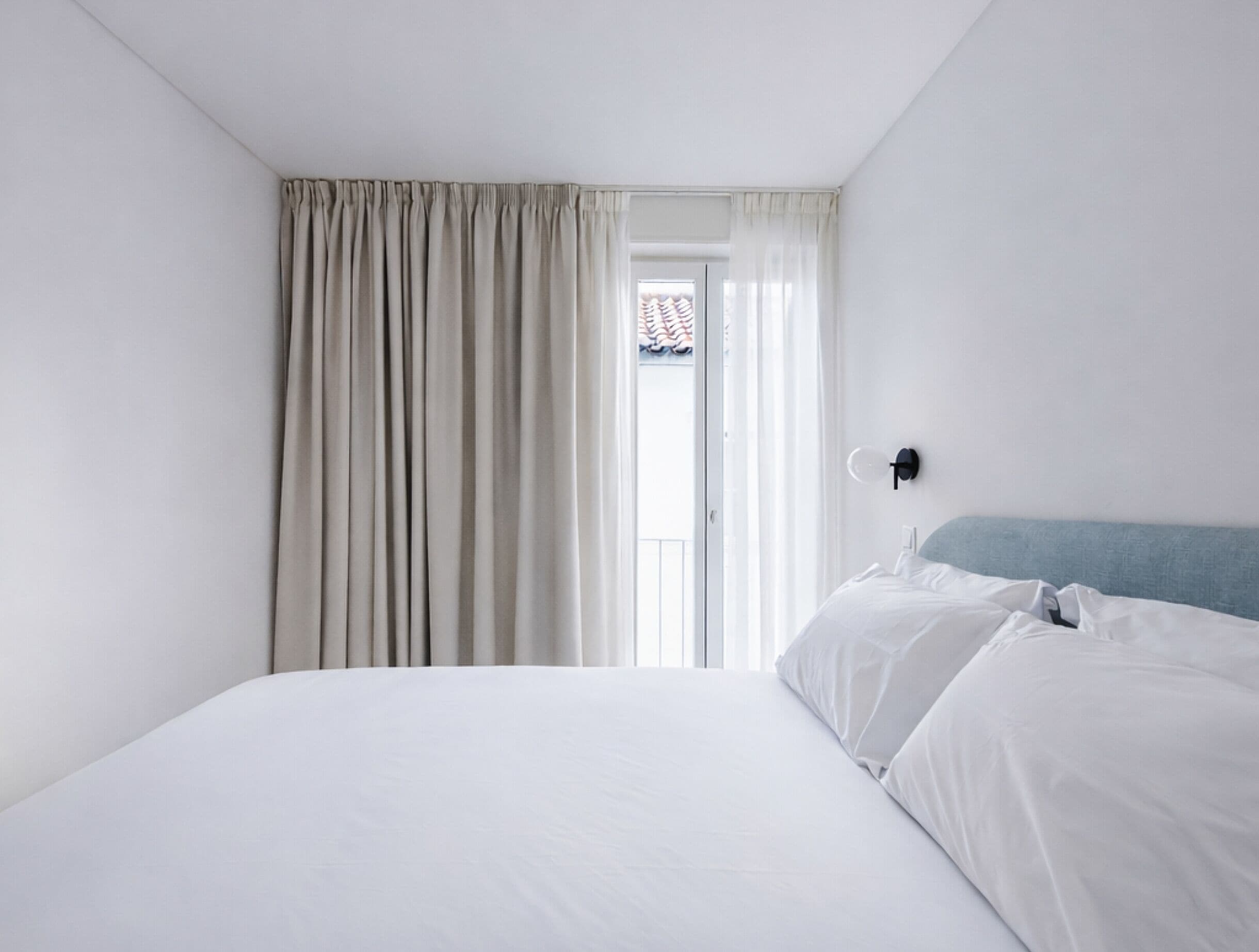Een hotelkamer met een bed, een raam met gordijnen en een wandlamp.
