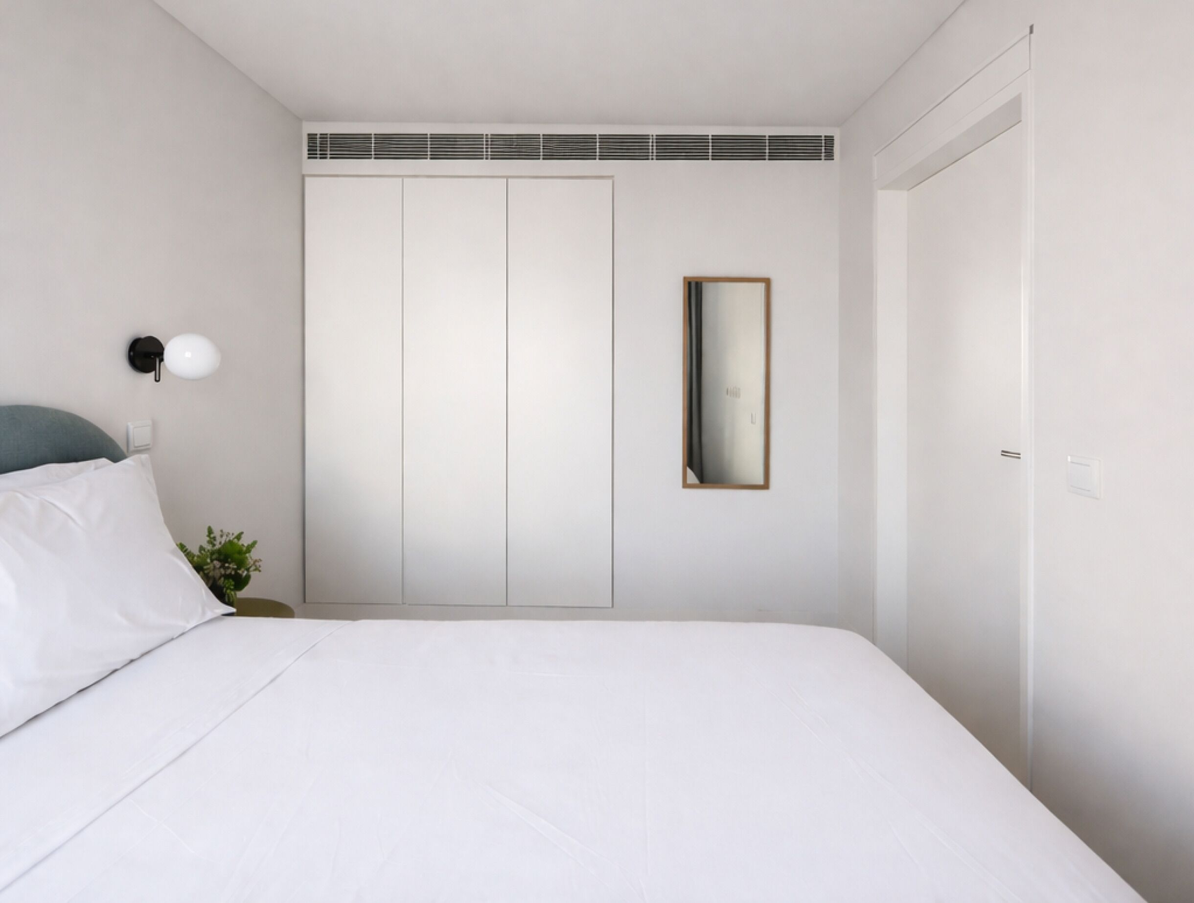 A bedroom with a bed, a nightstand, a wall-mounted mirror, and a wardrobe.