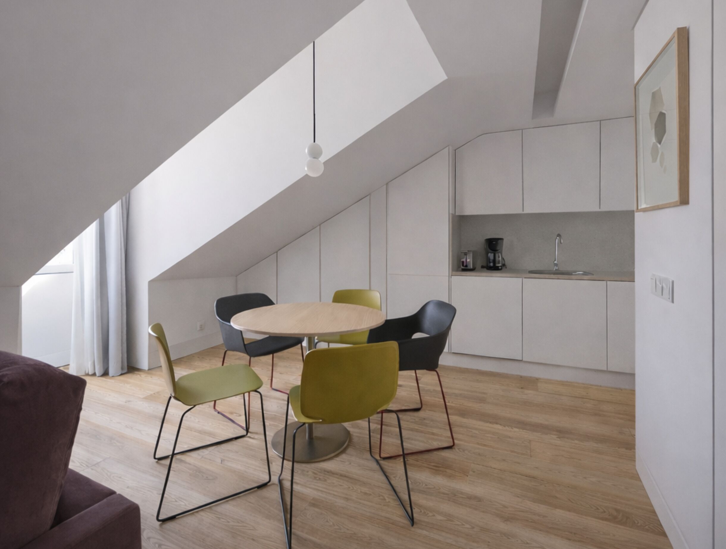 A modern kitchen with white cabinets, a dining area with a round table and four chairs, and a visible coffee maker.