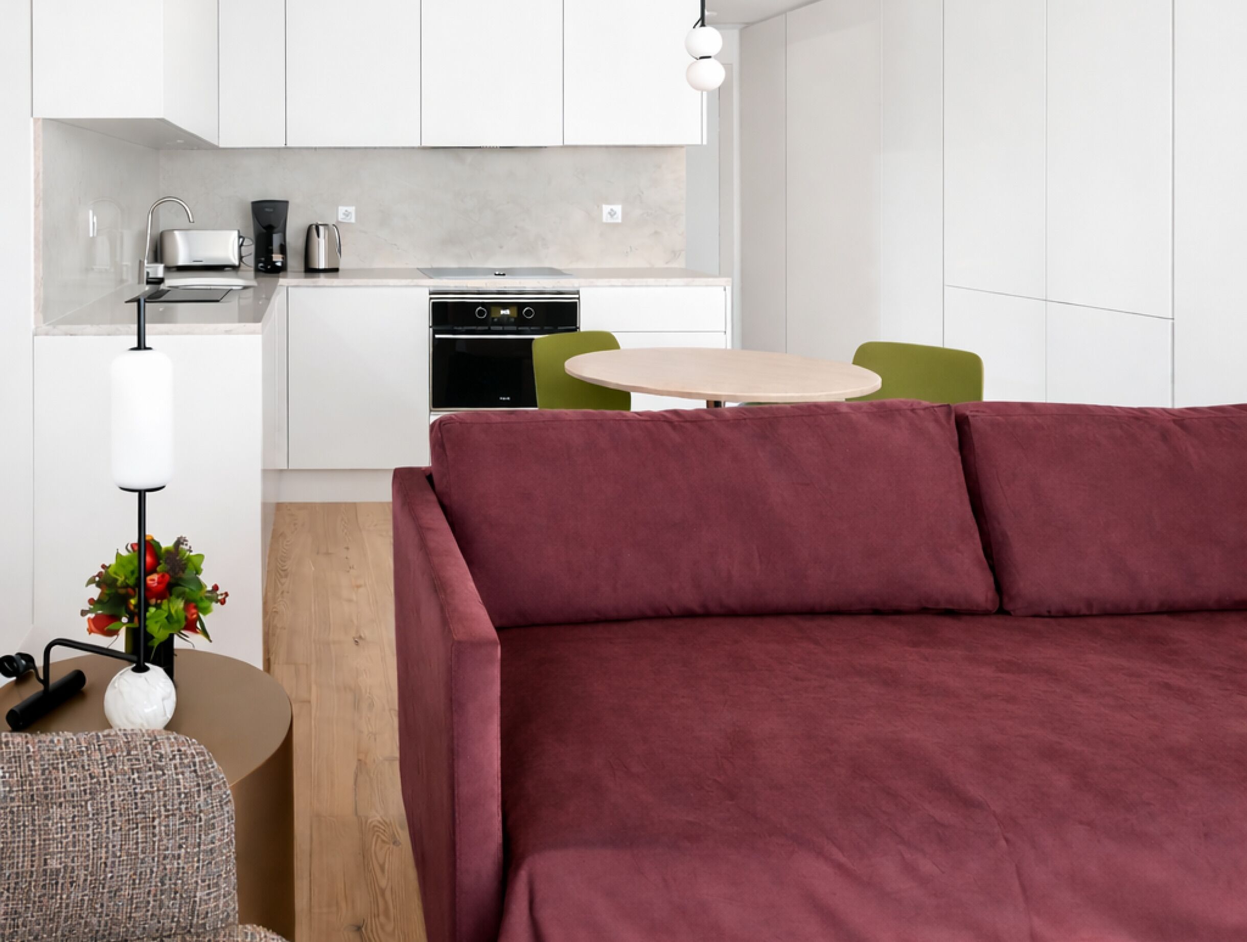 A modern living space with a sofa, a small round table, a coffee machine, and a kitchen area.