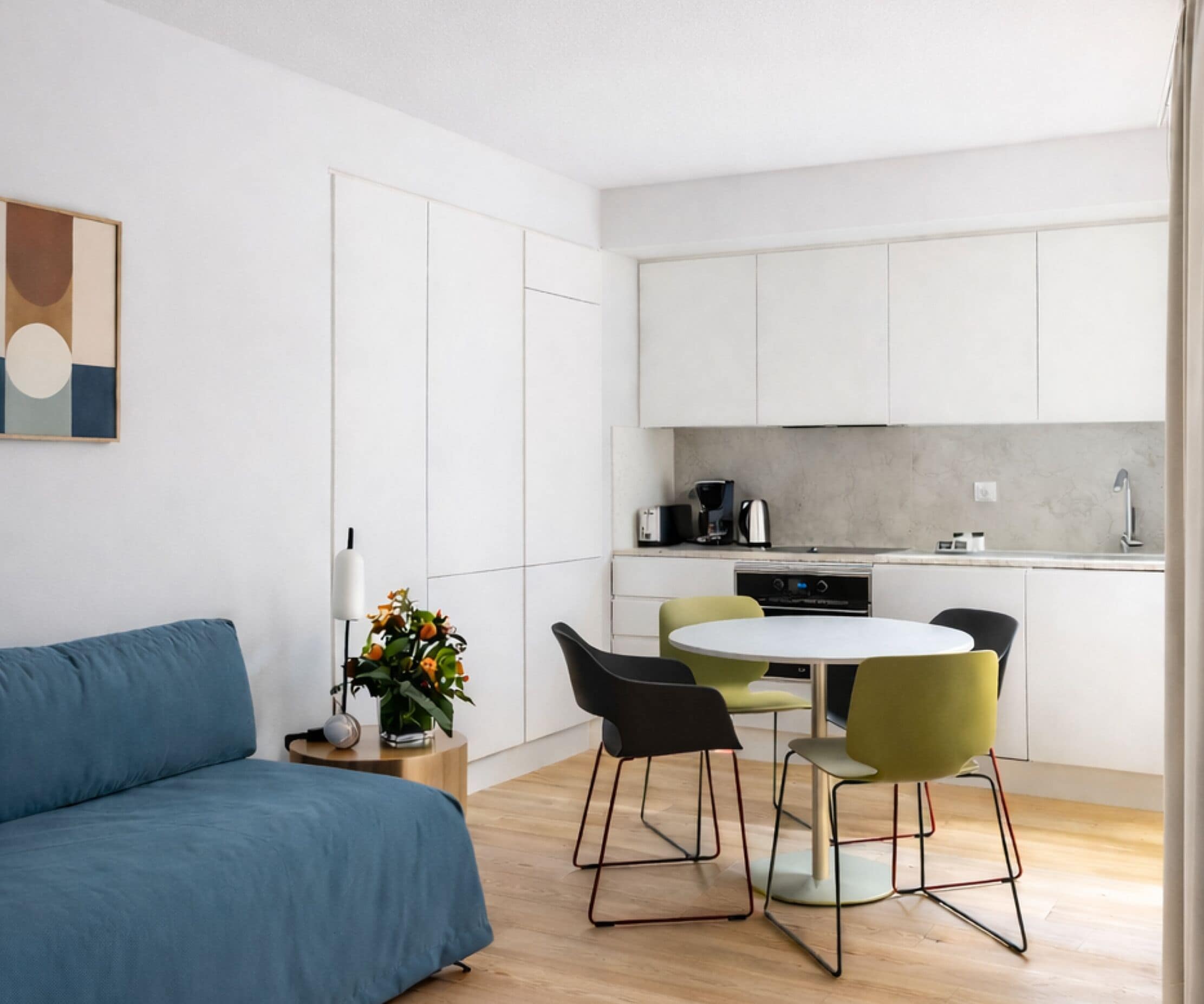 A modern kitchen with white cabinets, a round dining table, and a blue sofa.