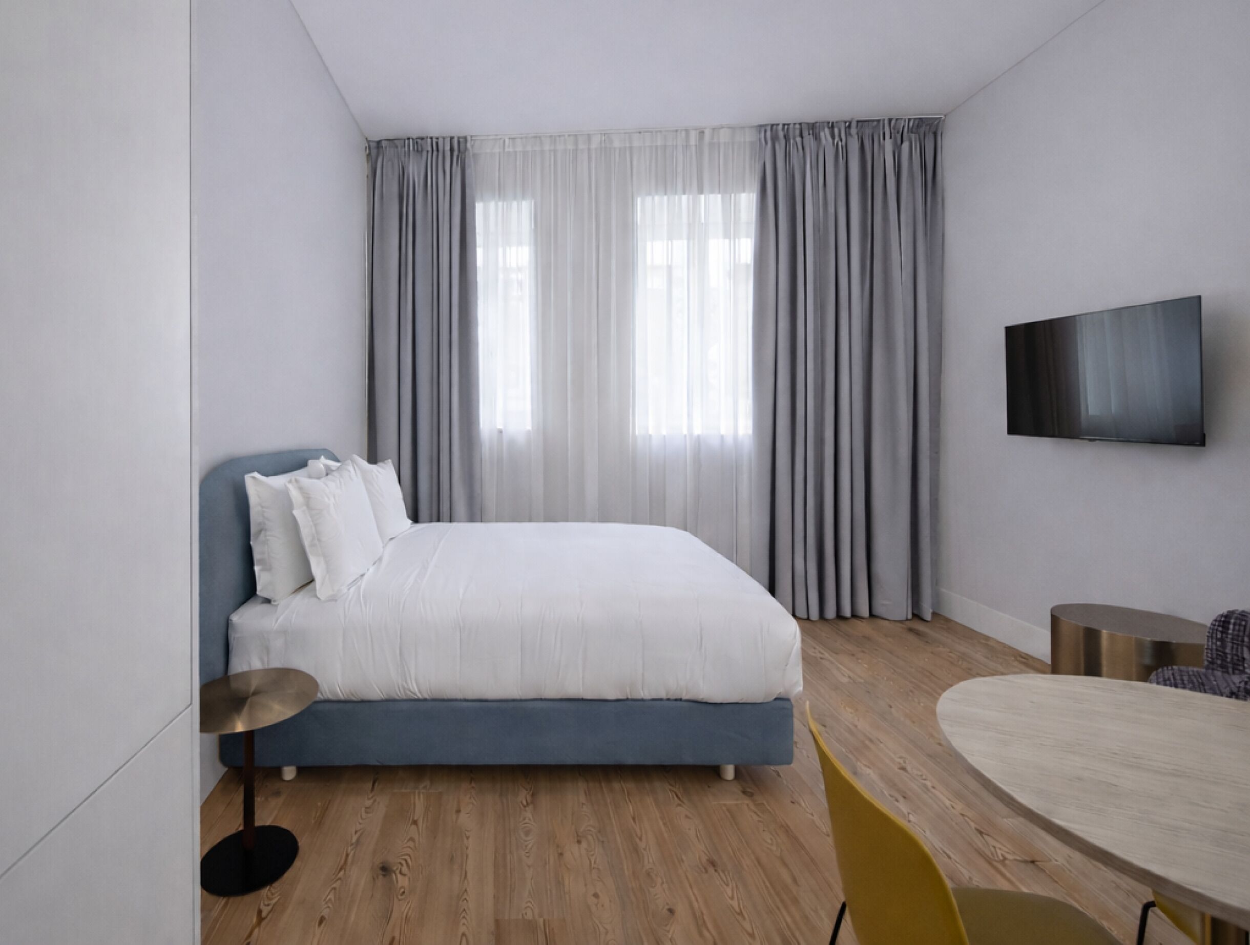 A modern bedroom with a bed, curtains, a TV, a round table, and a chair.