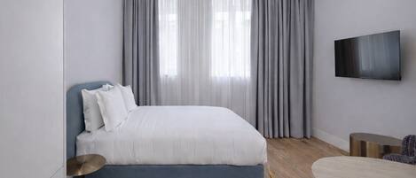 A modern bedroom with a bed, curtains, a TV, a round table, and a chair.