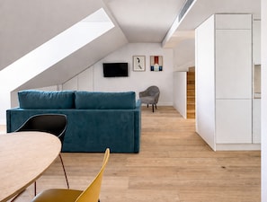Um apartamento loft moderno com teto inclinado, um sofá azul, uma mesa de jantar, uma cadeira, uma TV fixada na parede e uma escada.