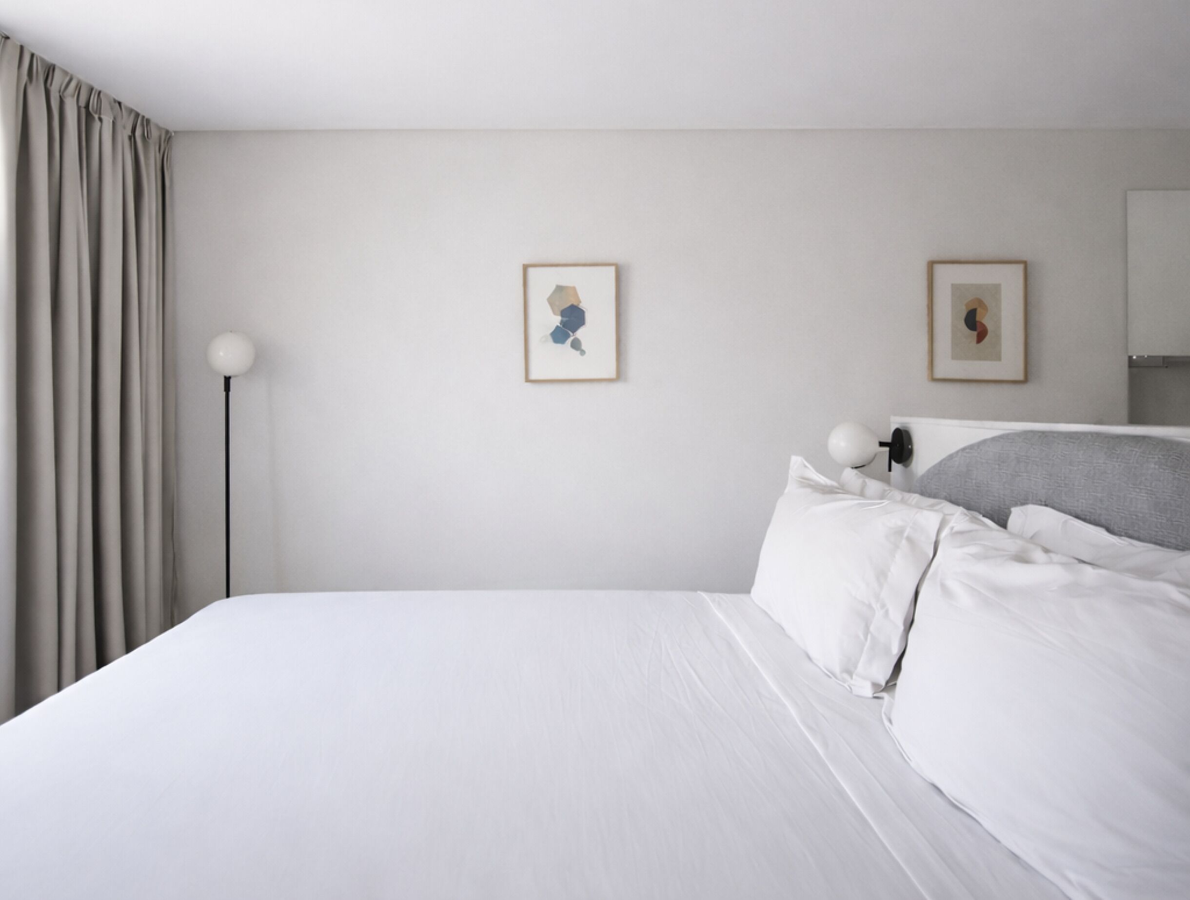 Habitación de hotel con una cama, una lámpara de pie y dos cuadros en la pared.
