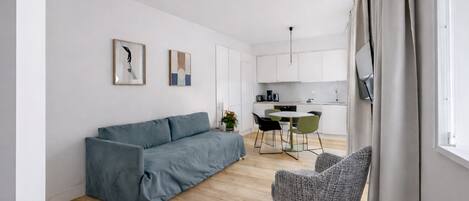 Ein modernes Wohnzimmer mit einer Couch, einem Sessel, einem Esstisch und einer Küchenzeile.