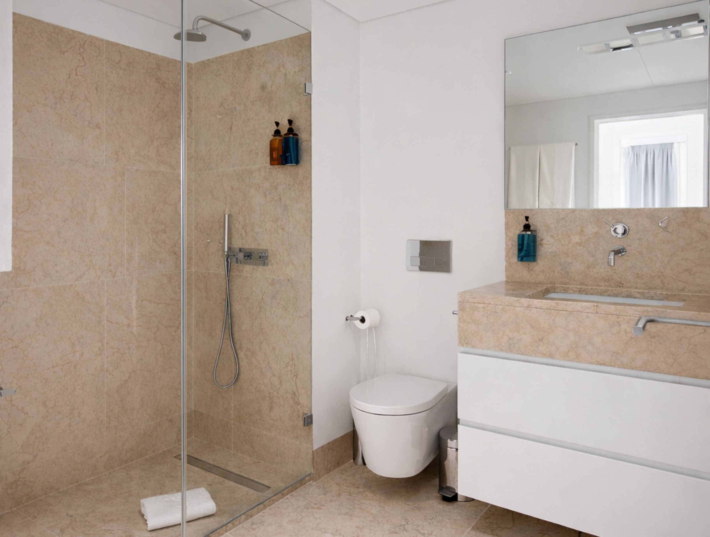 Un baño moderno con ducha envuelta en vidrio, inodoro y lavamanos con espejo.