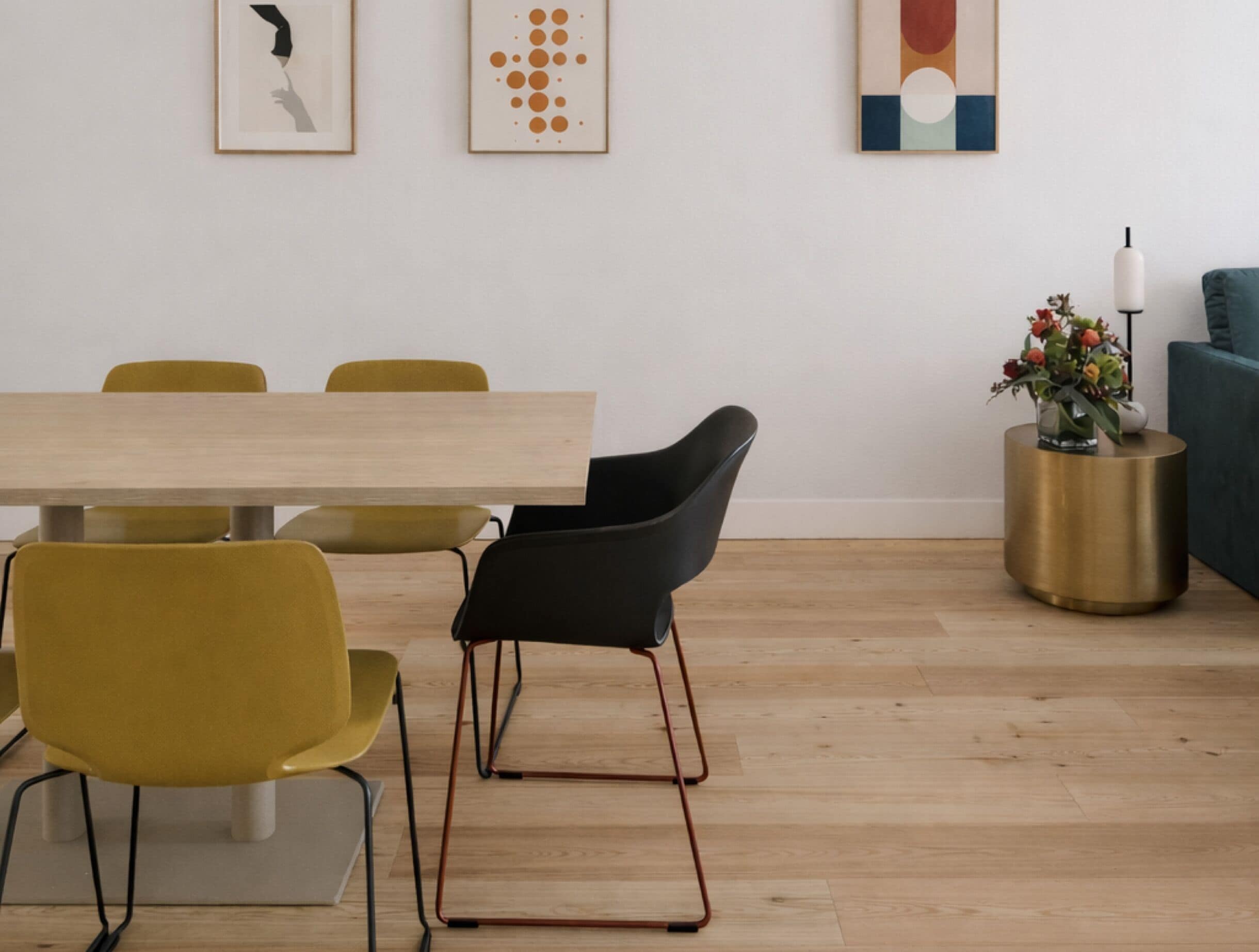 A dining area with a wooden table and chairs, a round gold side table with a vase, and abstract wall art.