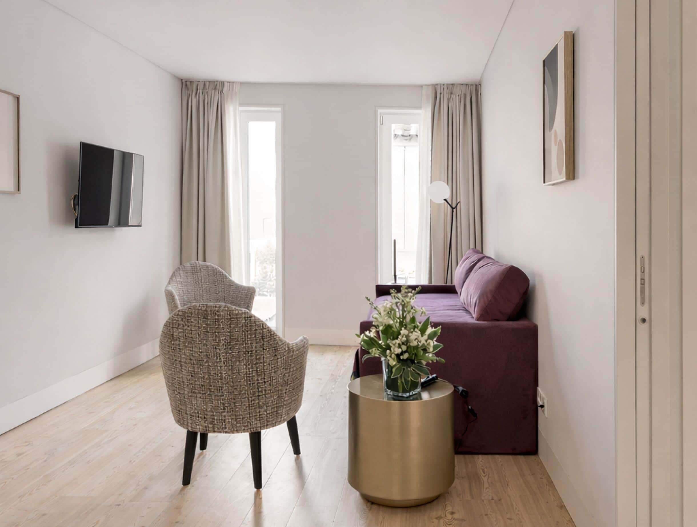 Una sala moderna con un sofá, una butaca, un televisor y un florero con flores.