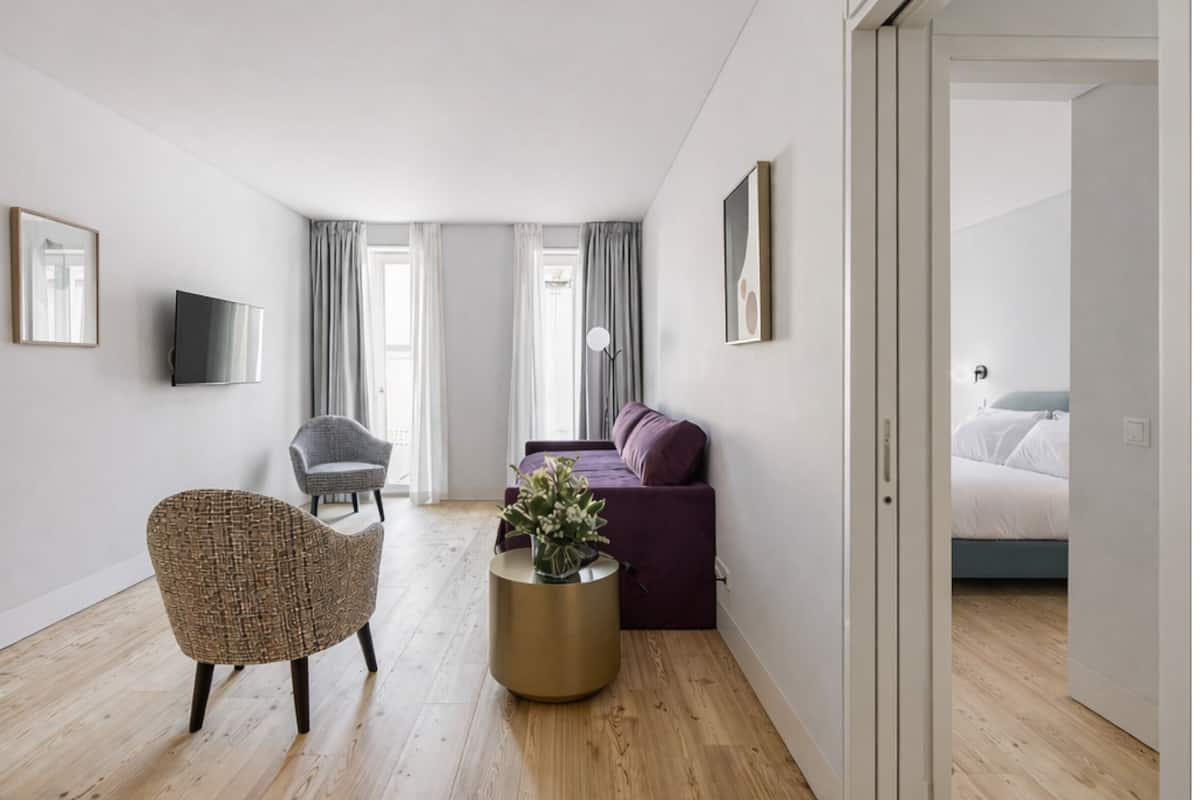 Una sala de estar moderna con un sofá, una silla, una mesa redonda con un florero y un televisor montado en la pared.