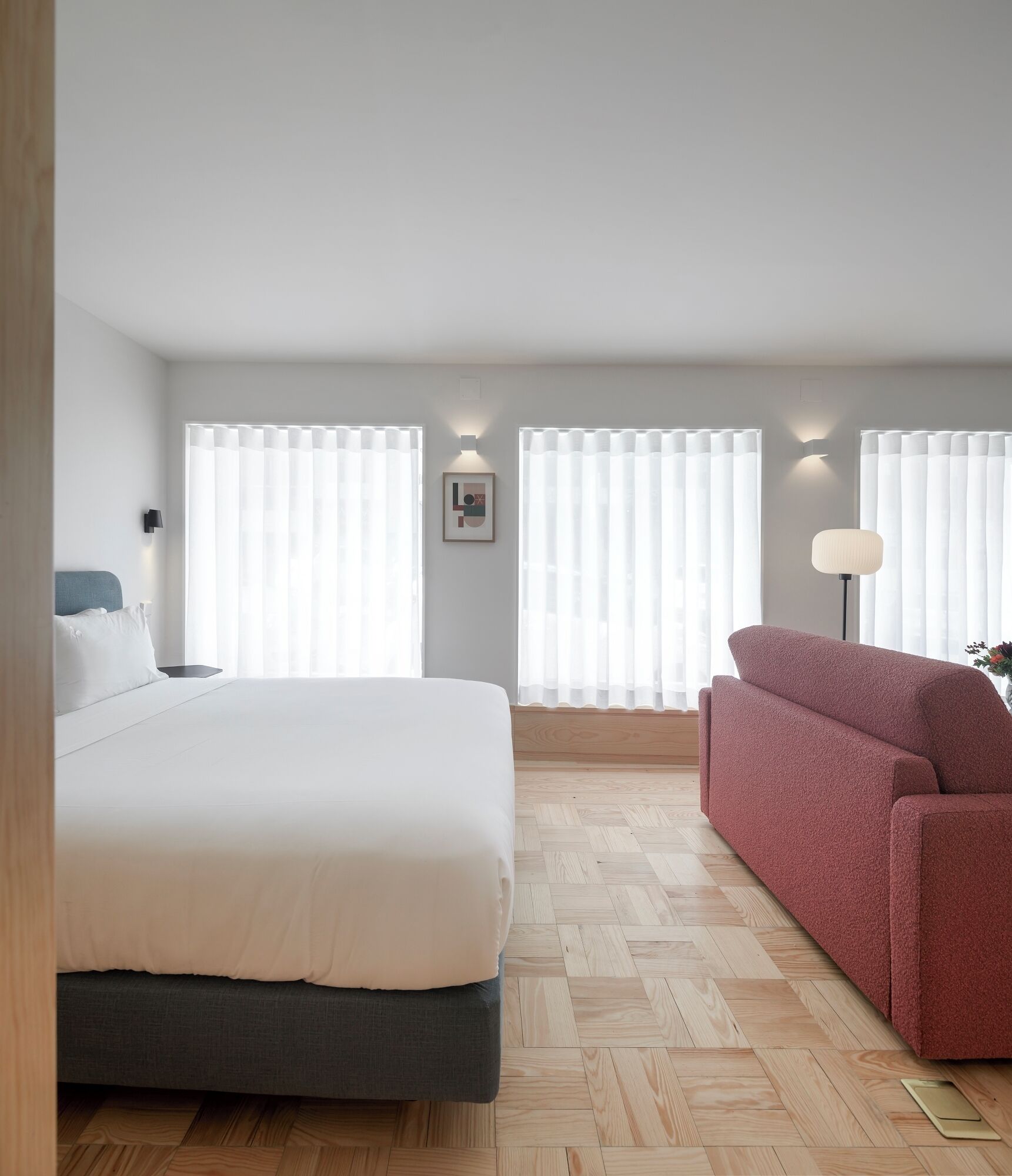A bedroom with a bed, a red sofa, a nightstand, a lamp, and a picture on the wall.