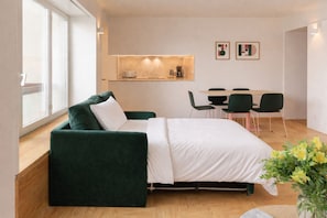 Une chambre moderne avec un canapé vert, un lit, une table à manger avec des chaises et une petite kitchenette.