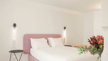 A bedroom with a bed, a bedside table, a nightstand, a lamp, and a vase with flowers.