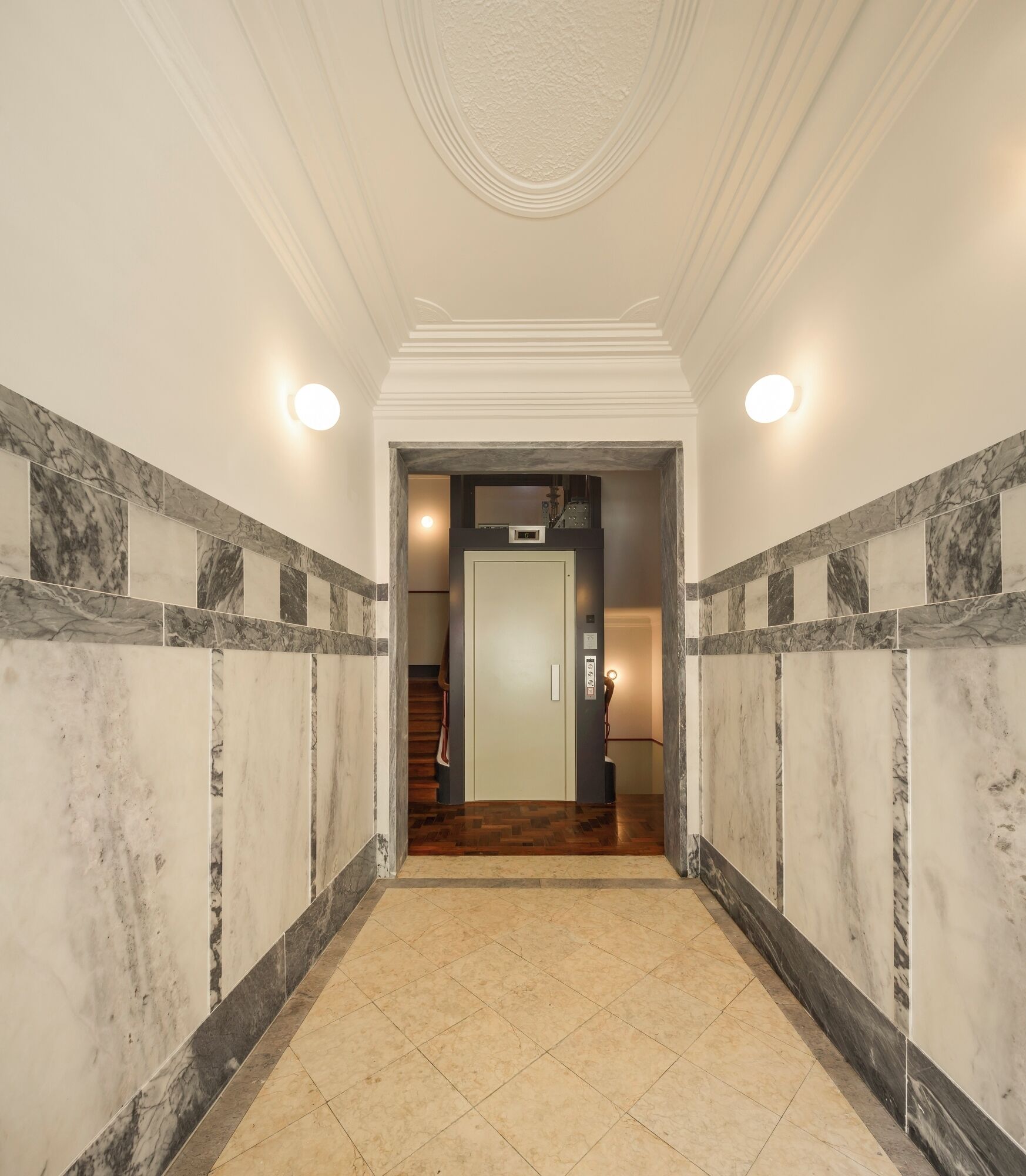 A hallway with marble walls, a wooden staircase, and a door at the end.