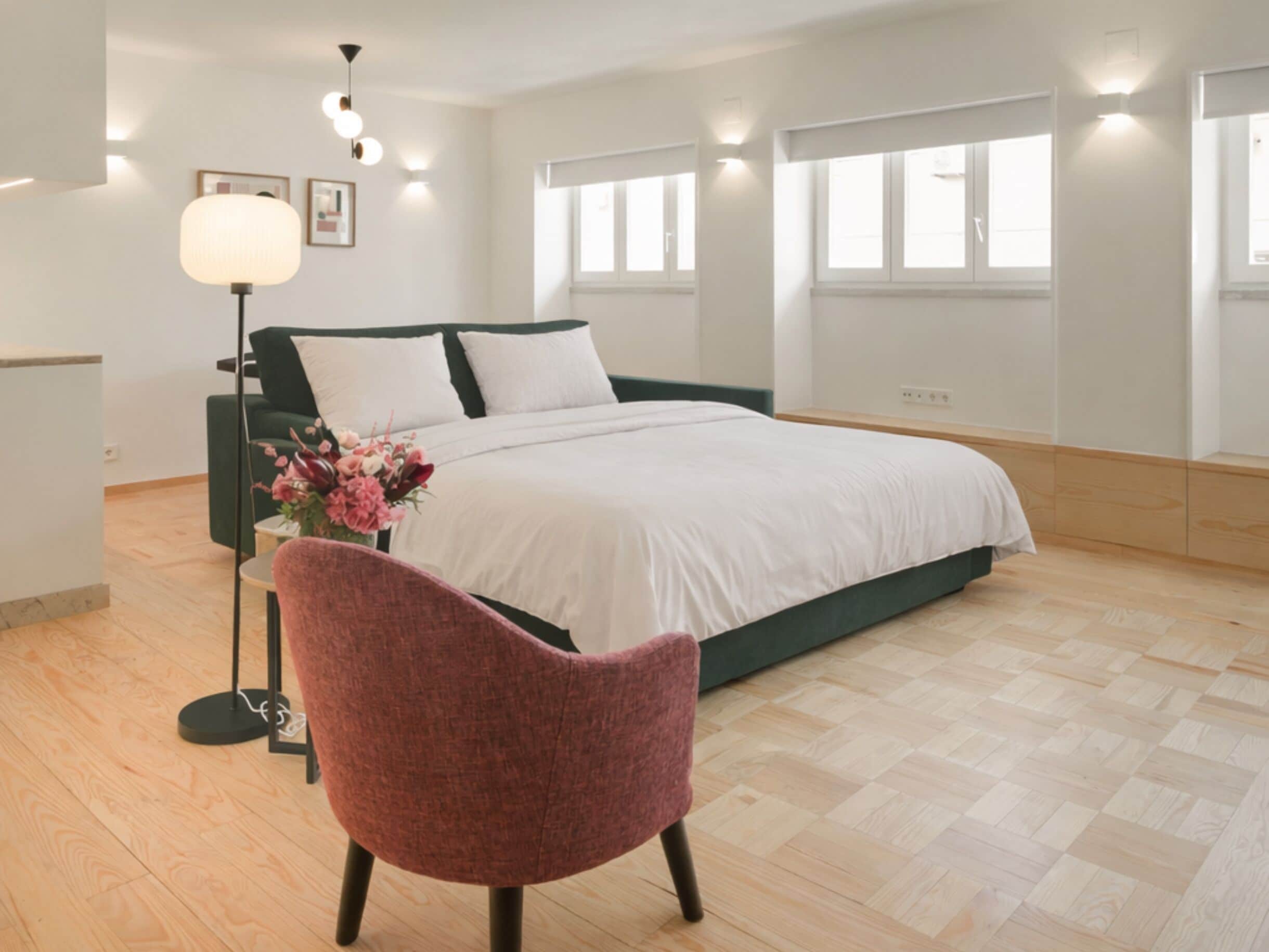 A modern bedroom with a bed, a chair, a floor lamp, and a window.
