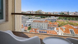 A balcony with a view of a cityscape, including buildings with red-tiled roofs and a clear blue sky.