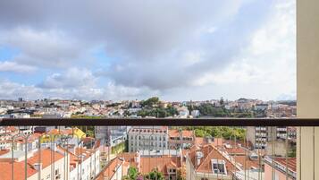 Un balcon offrant une vue sur le paysage urbain, avec des bâtiments aux toits recouverts de tuiles rouges et un ciel nuageux.