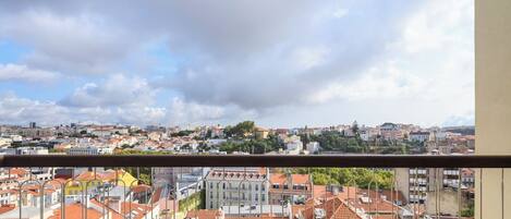 Un balcón con vista a un paisaje urbano, incluyendo edificios con techos de tejas rojas y un cielo nublado.