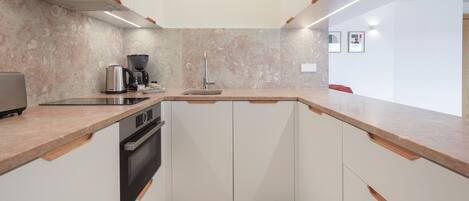 A modern kitchen with white cabinets, a built-in oven, a coffee maker, and a sink.