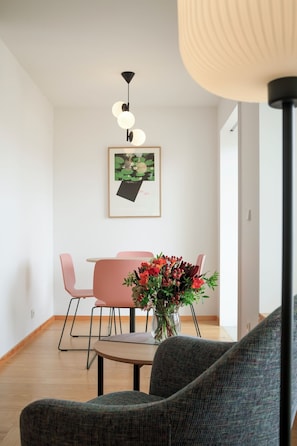 Un salon moderne avec un coin repas, une œuvre d’art encadrée au mur et un vase de fleurs posé sur une table.