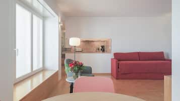 A modern living room with a dining table, a red sofa, a small kitchen area, and a large window.