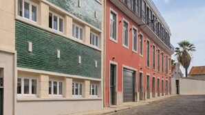 A multi-story building with a green-tiled facade, a red building with balconies, and a cobblestone street.