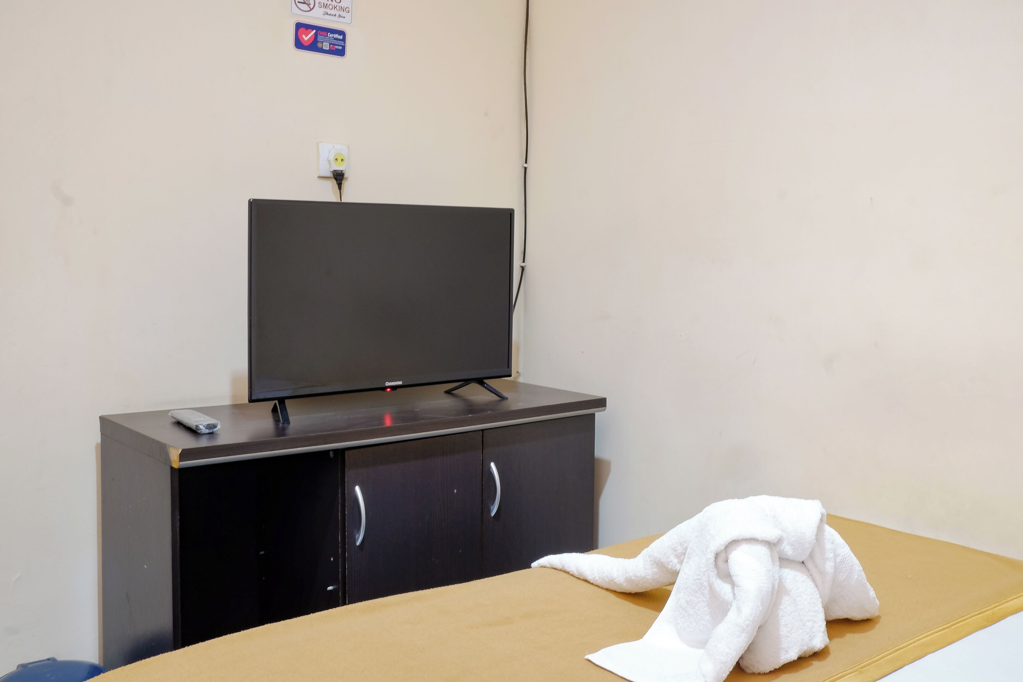 Ein Zimmer mit Fernseher auf einem Schrank, einer Fernbedienung und einem weißen Handtuch auf dem Bett.