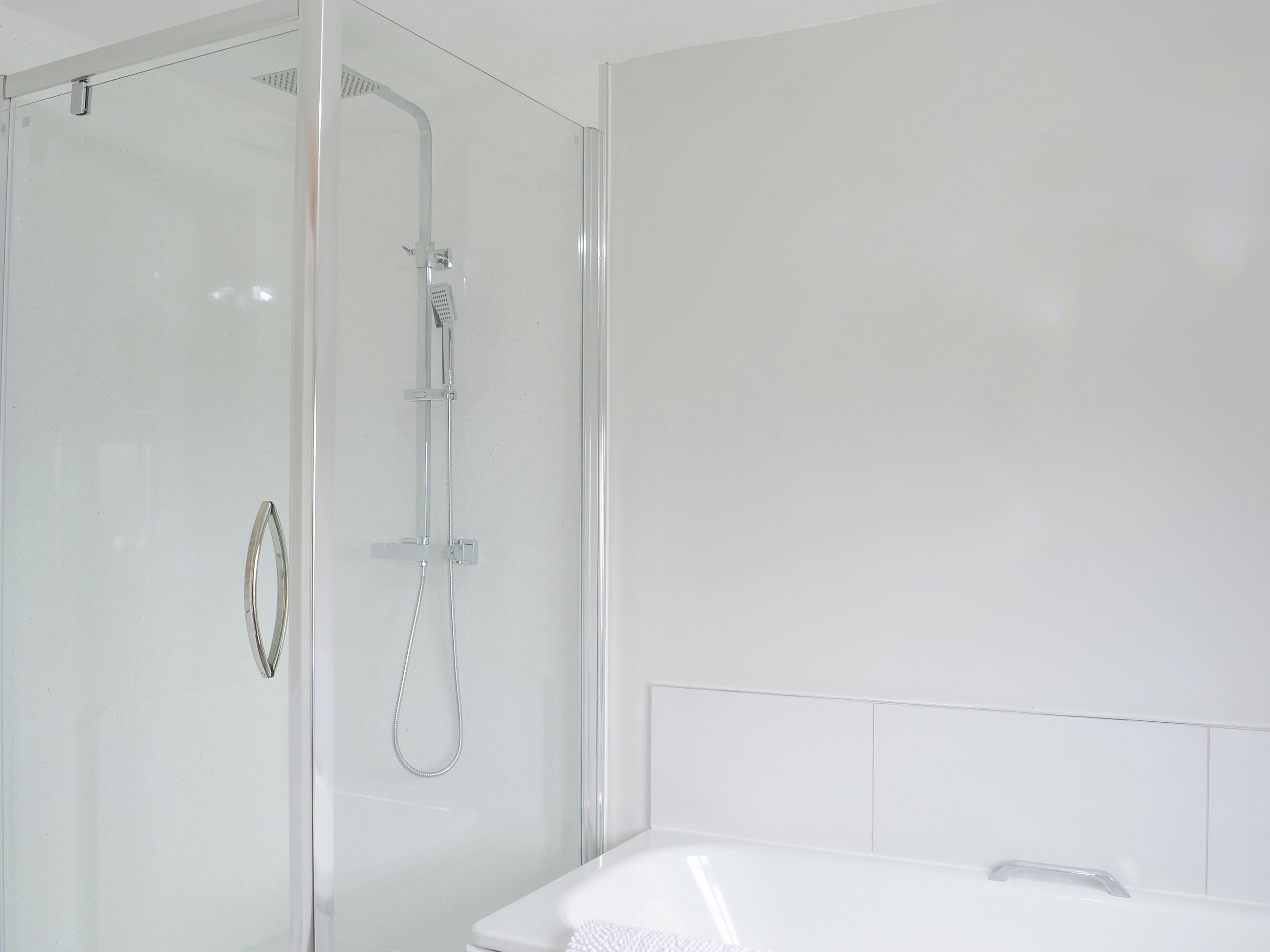 Un bagno moderno con doccia vetrata, una vasca da bagno bianca e una parete bianca e liscia.