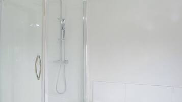 Un bagno moderno con doccia vetrata, una vasca da bagno bianca e una parete bianca e liscia.