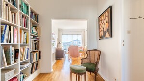A hallway with a bookshelf, a wicker chair, and a view to a living area. - La Belle Vue - 65m2 au dernier étage avec ascenseur (Marseille)
