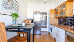 A compact kitchen with wooden cabinets, a stainless steel refrigerator, a washing machine, and a dining area with a table and chairs. - La Belle Vue - 65m2 au dernier étage avec ascenseur (Marseille)