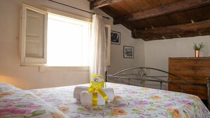 Une chambre à coucher avec un lit, un plafond en bois, une fenêtre avec des rideaux, une commode et une petite plante.