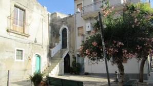 Une cour avec un banc vert, un arbre aux fleurs roses et un bâtiment doté d’un escalier.