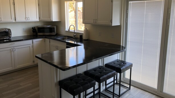 A modern kitchen with white cabinets, a black countertop, a built-in oven, a microwave, and a window with a view.